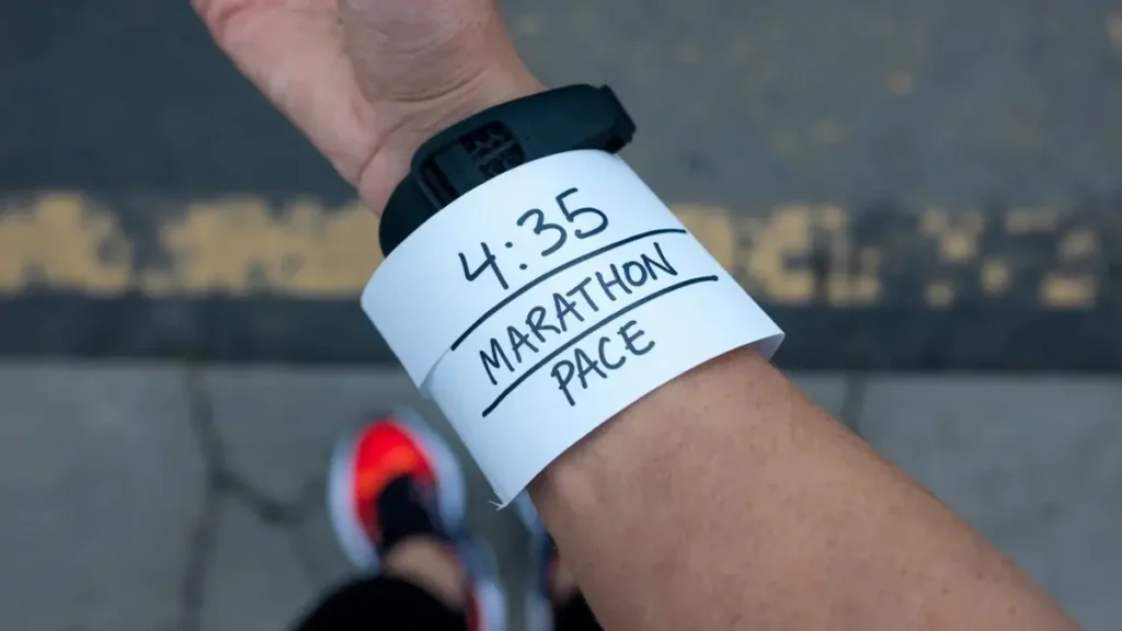 a piece of paper that has been wrapped around the wrist of a runner. the paper is blank, white, but has the words "4:35 Marathon Pace" written on it in pen. the image is POV of the runner.