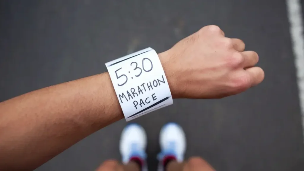 a piece of paper that has been wrapped around the wrist of a runner. the paper is blank, white, but has the words "5:30 Marathon Pace" written on it in pen. the image is POV of the runner.