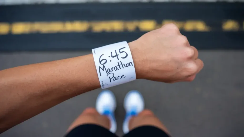 a piece of paper that has been wrapped around the wrist of a runner. the paper is blank, white, but has the words "6:45 Marathon Pace" written on it in pen. the image is POV of the runner.