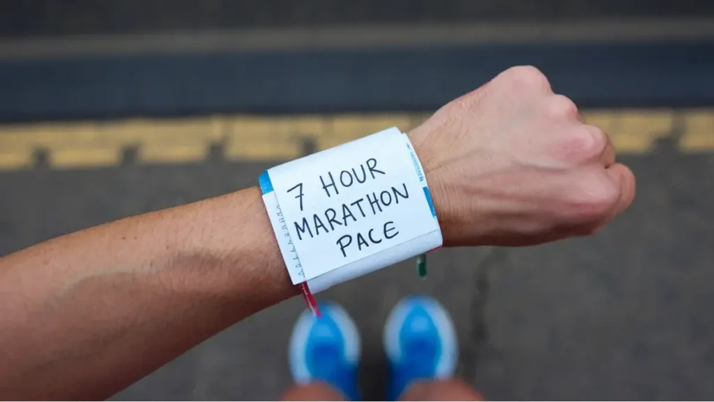 a piece of paper that has been wrapped around the wrist of a runner. the paper is blank, white, but has the words "7:00 Marathon Pace" written on it in pen. the image is POV of the runner.