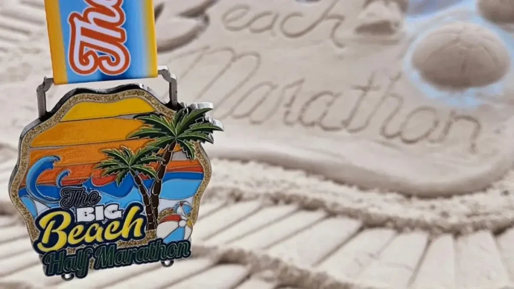 A Big Beach Marathon finisher’s medal held in front of a sandcastle in Gulf Shores