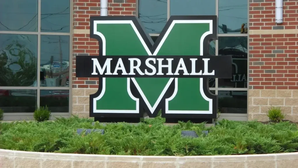 Large green Marshall University sign in front of a brick building, representing the Marshall University Marathon.